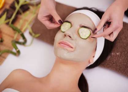 Woman with clay facial mask in beauty spa. In background tropical plants